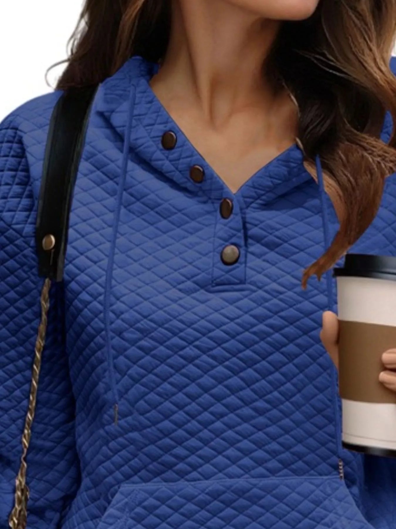 Person wearing a blue quilted jacket holding a coffee cup.