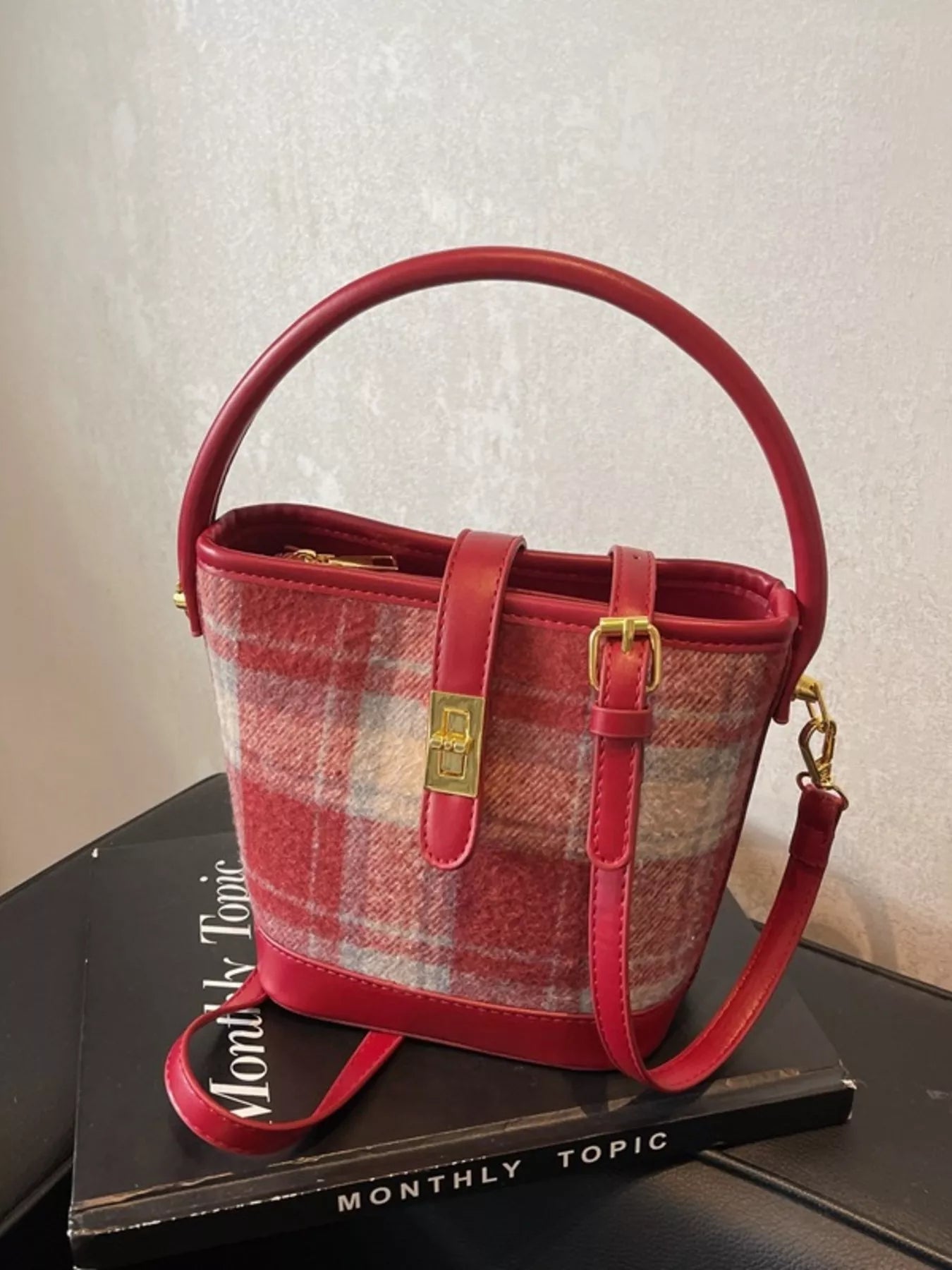 Red plaid handbag with gold accents on a black surface