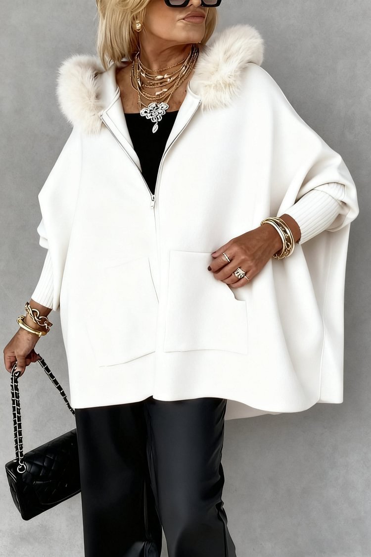 Person wearing a white coat with fur hood, black pants, and holding a black handbag on a gray background.