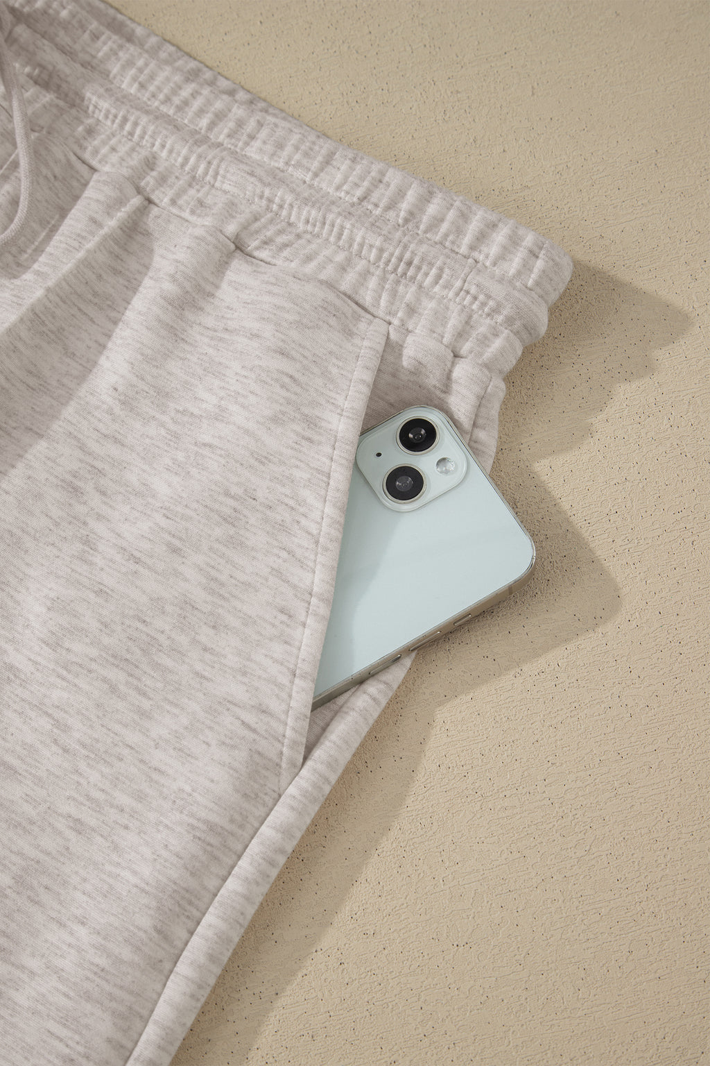 Light gray sweatpants with a light blue phone peeking out from the pocket on a beige surface