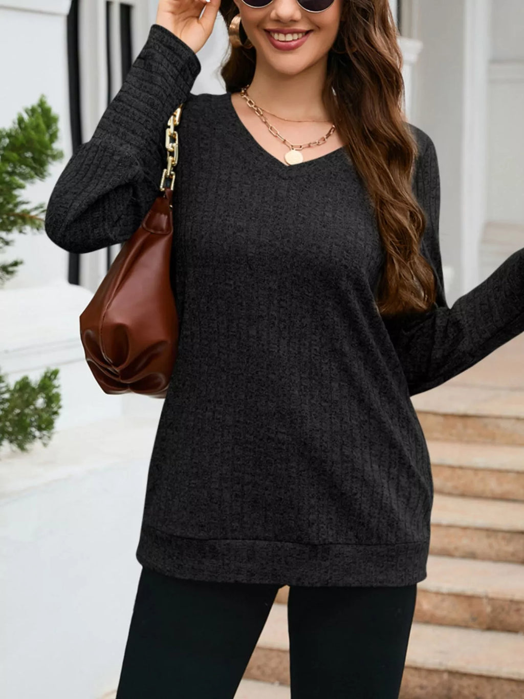 Woman wearing a dark gray sweater and holding a brown bag on a staircase.