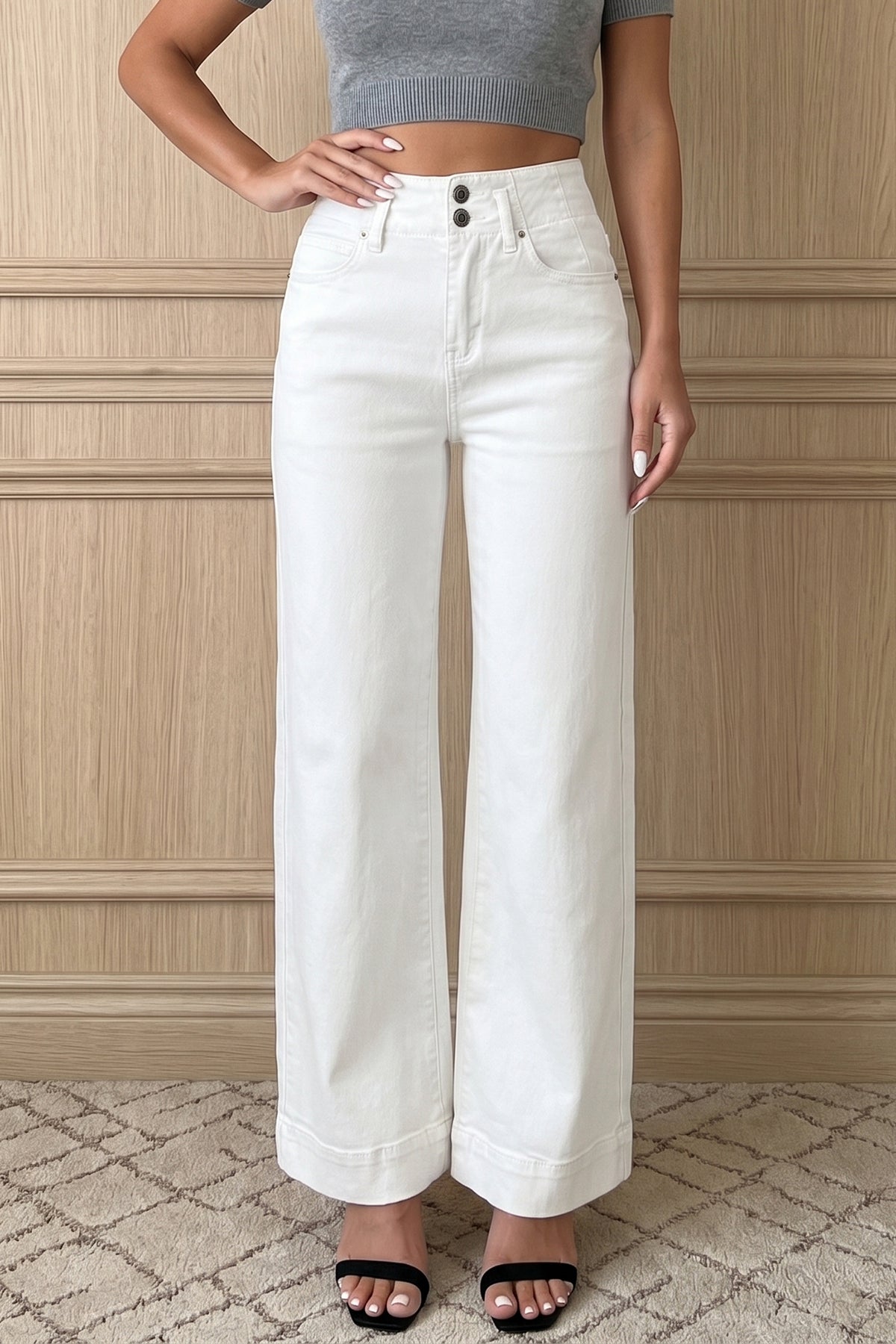 A model wearing a pair of  white High Waist Wide Leg Jeans with a double-button waistband, paired with a gray crop top and black slide sandals.
