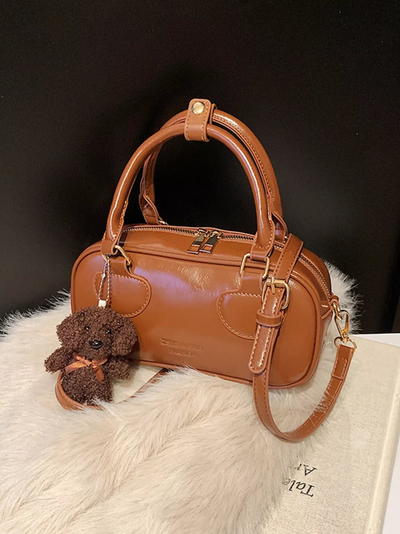 Brown handbag with a teddy bear charm on a white fur surface