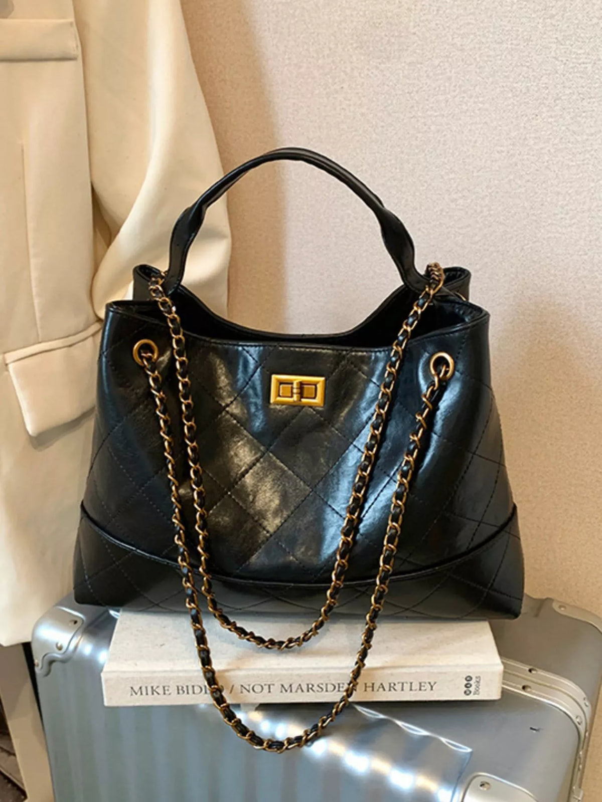 Black quilted handbag with gold chain strap on a suitcase