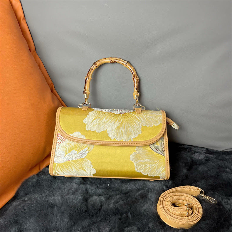 Yellow handbag with floral design and bamboo handle on a gray background