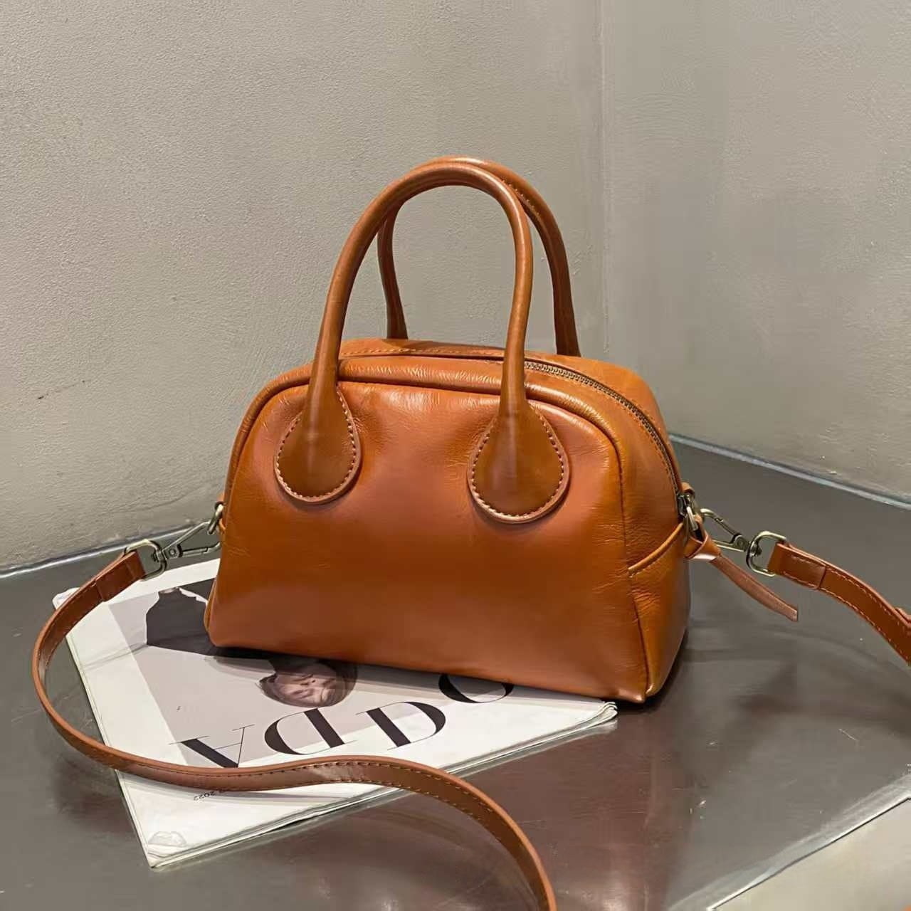 Brown leather handbag on a reflective surface with a magazine underneath