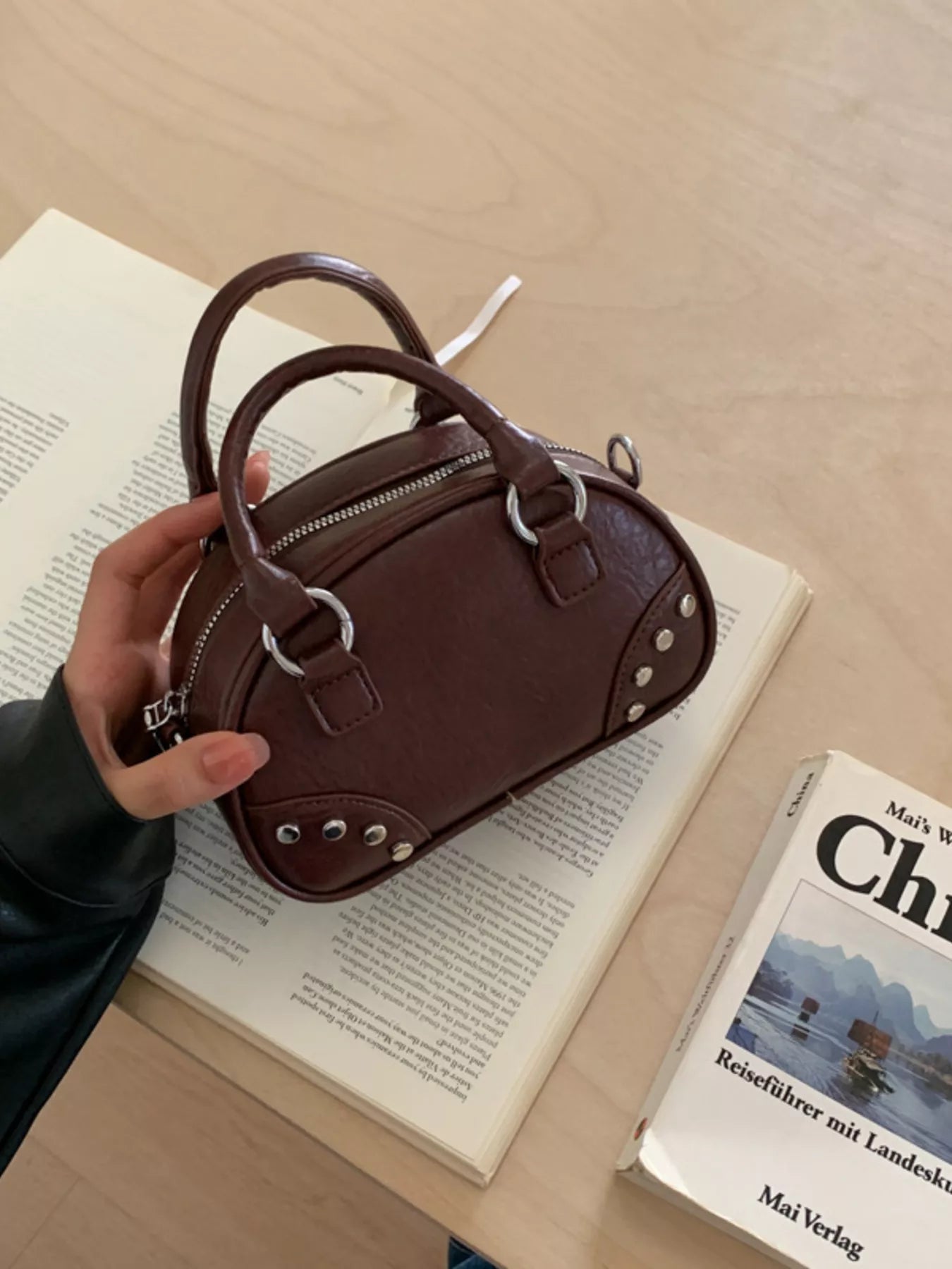 Brown leather handbag held over an open book with a visible book titled 'Ch'.
