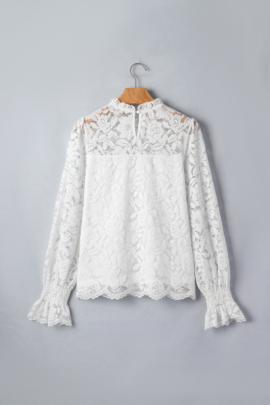 White lace blouse on a wooden hanger against a gray background front view