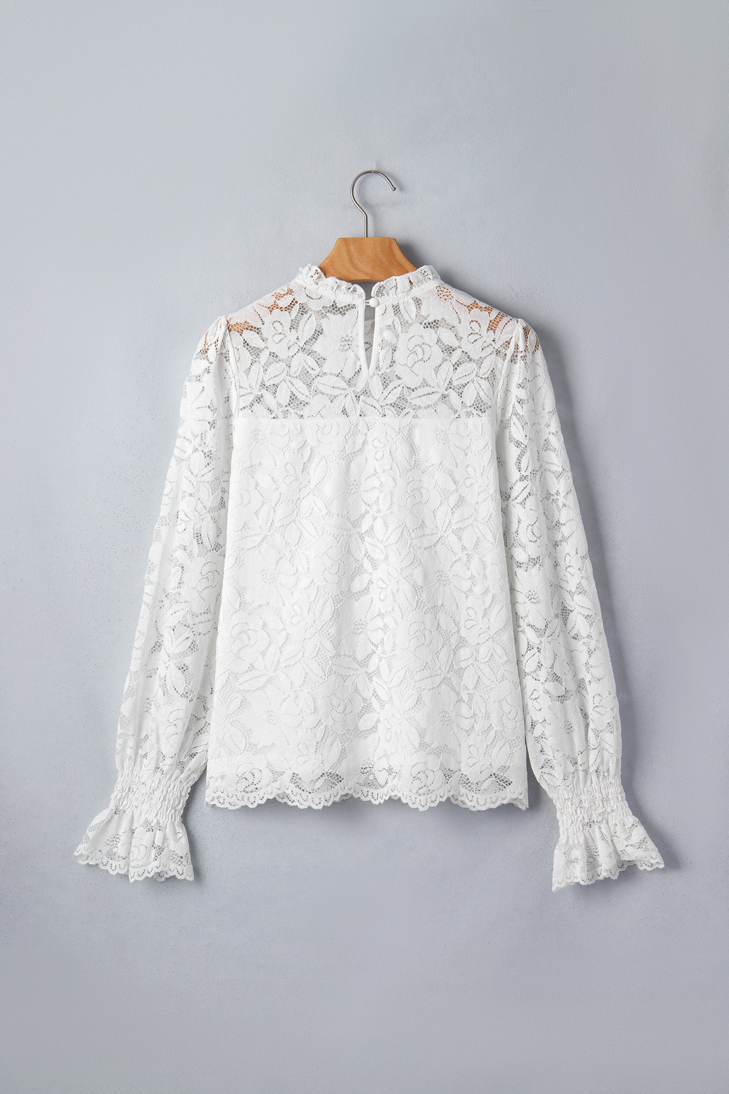 White lace blouse on a wooden hanger against a gray background front view