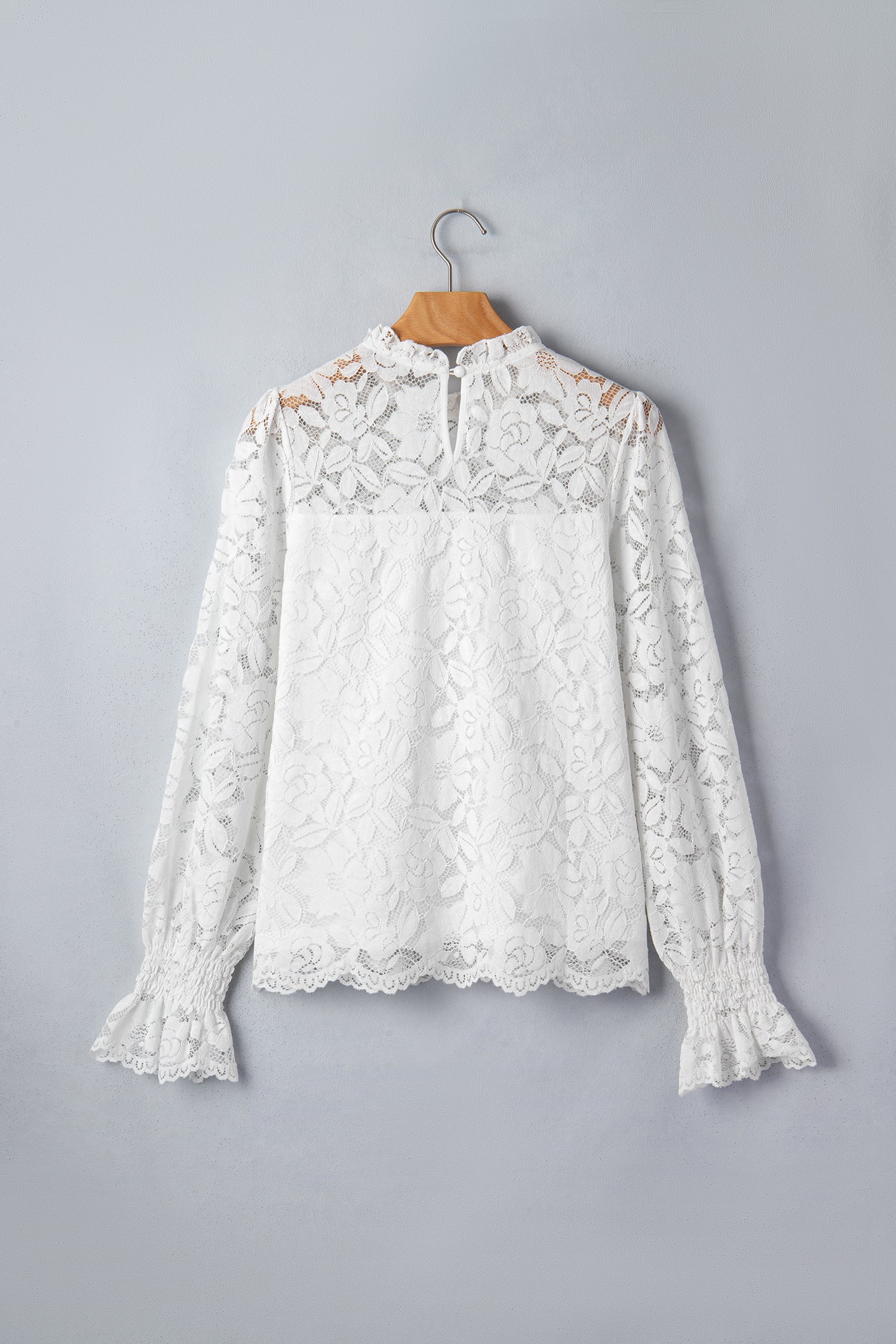 White lace blouse on a wooden hanger against a gray background front view