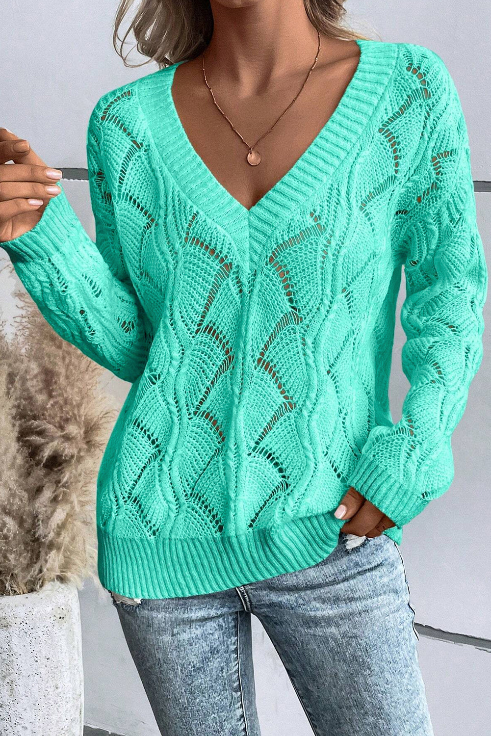 Person wearing a green knitted sweater with a neutral background