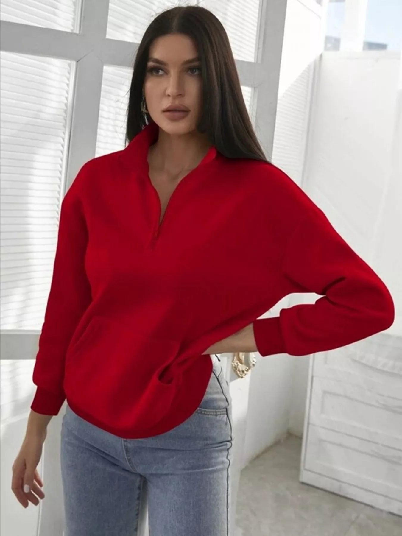 Woman wearing a red sweater and light blue jeans indoors.