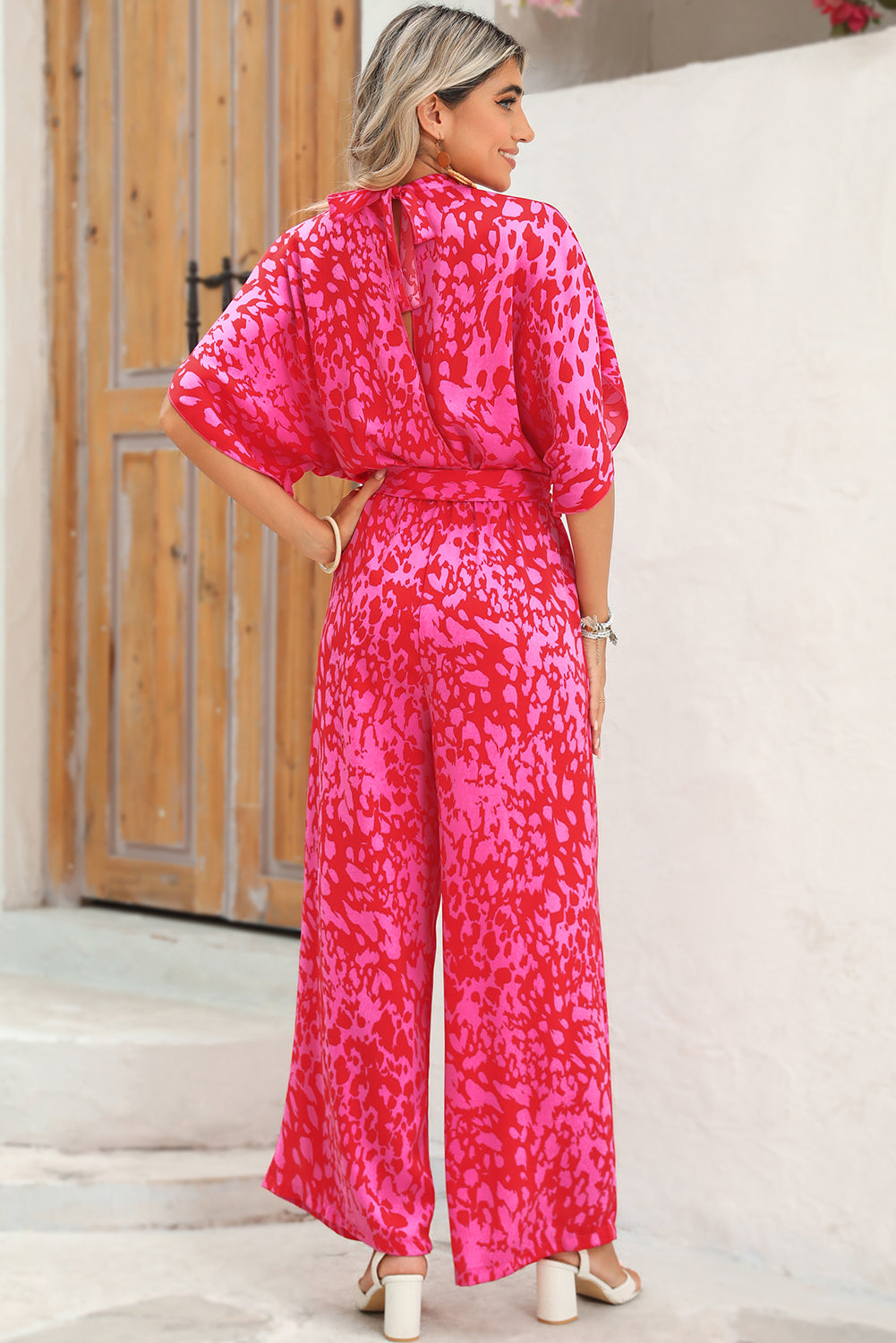 Woman wearing a pink patterned jumpsuit standing against a white wall.