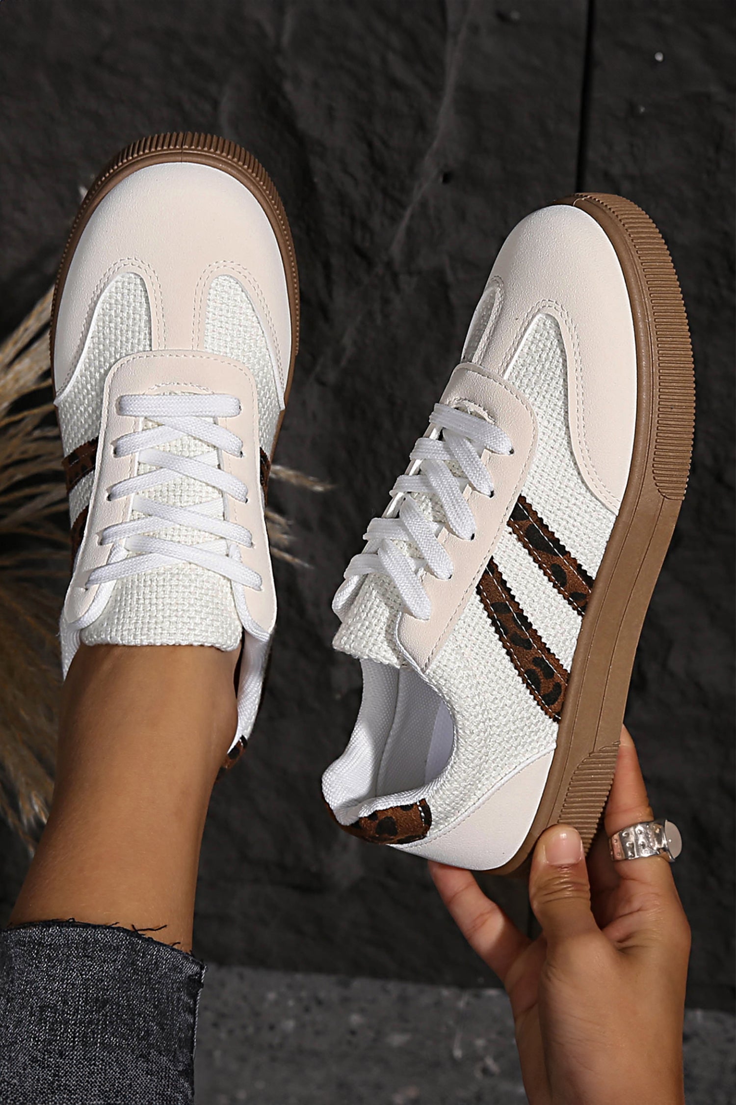 White sneakers with brown soles held by a person against a dark background