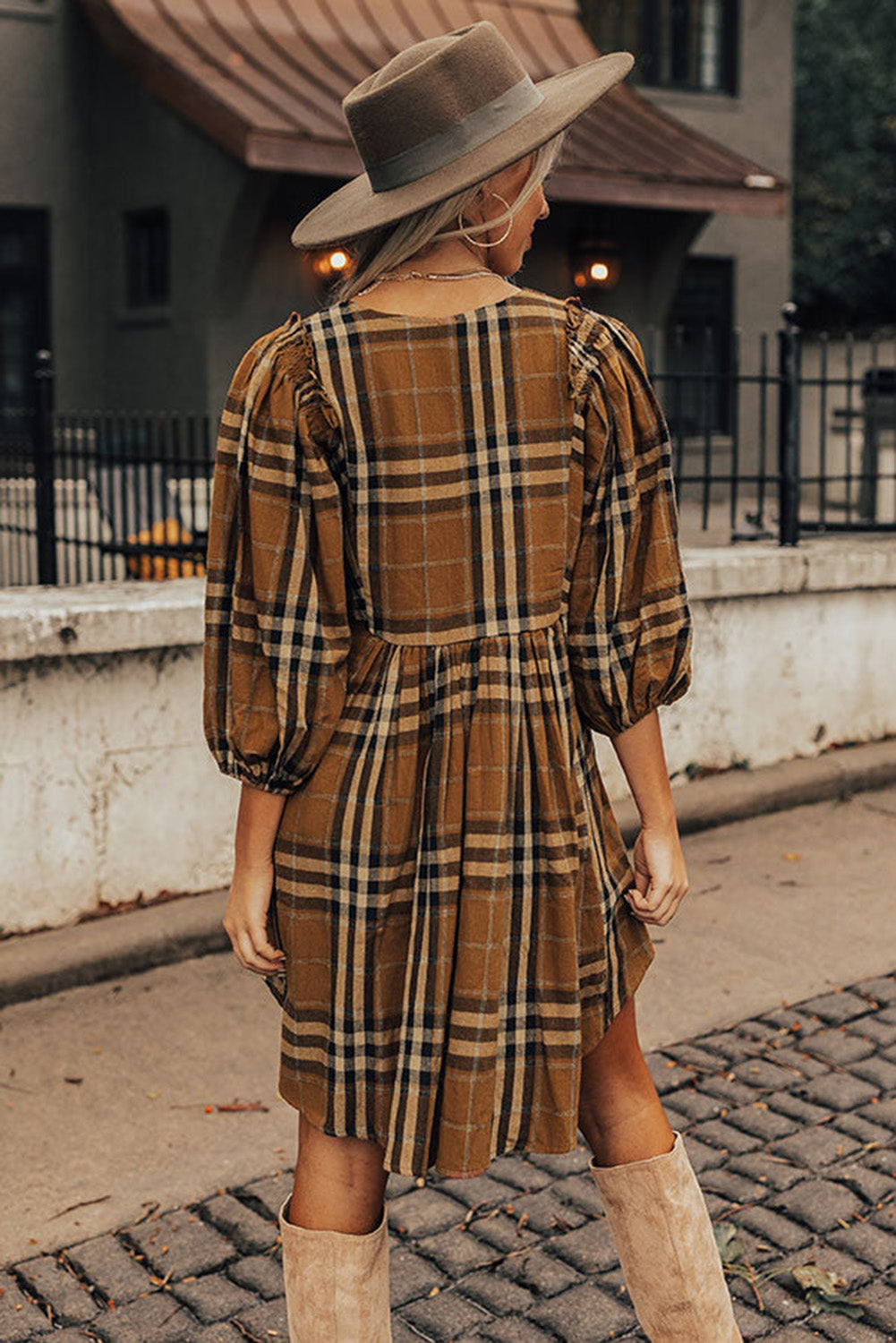 Woman wearing a plaid dress and hat on a street.