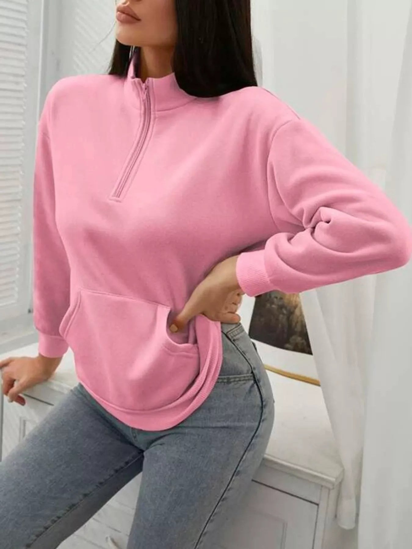 Person wearing a pink sweatshirt with a zipper and gray jeans indoors.