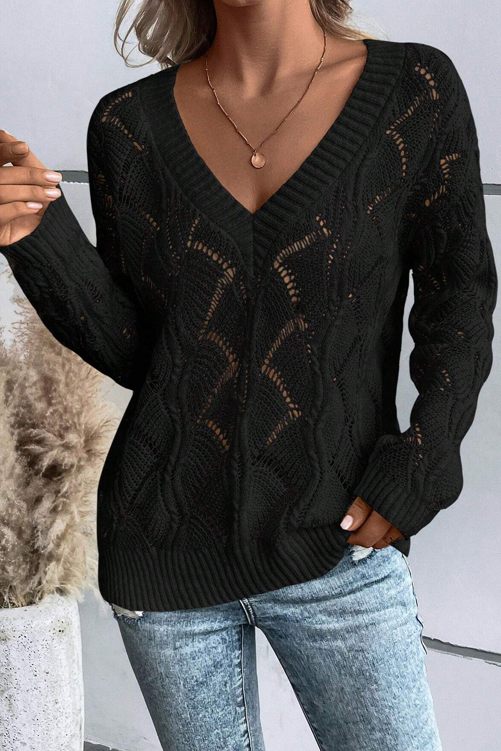 Person wearing a black cable knit sweater and light blue jeans against a neutral background