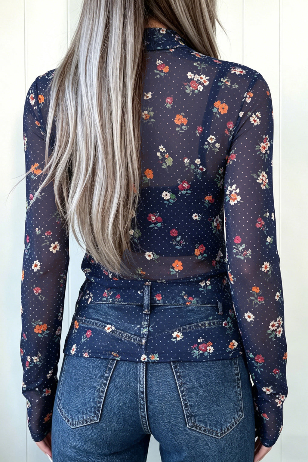 A woman viewed from the back wearing a Chic Women's Blue Polka Dot Floral Sheath Top over a dark navy base, paired with blue jeans against a white paneled wall.