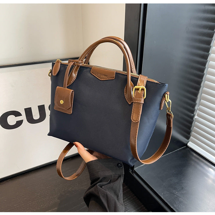 Blue handbag with brown leather straps and handle held by a person against a blurred background.