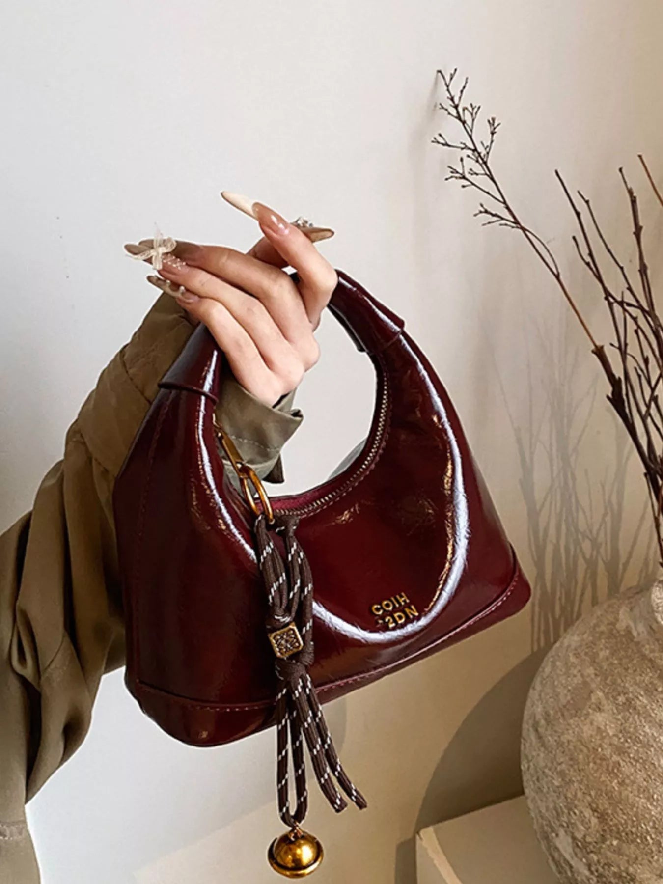 Brown handbag with decorative tassel held by a hand against a neutral background