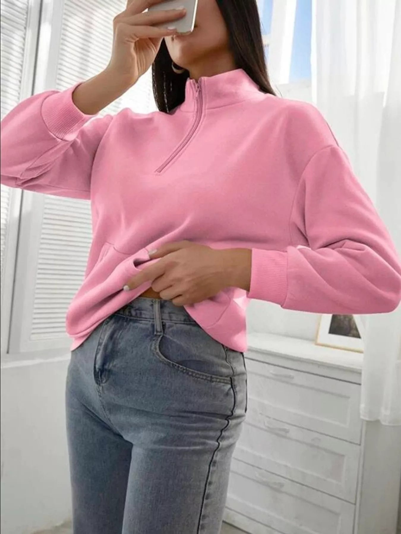 Person wearing a pink fleece pullover and blue jeans indoors.