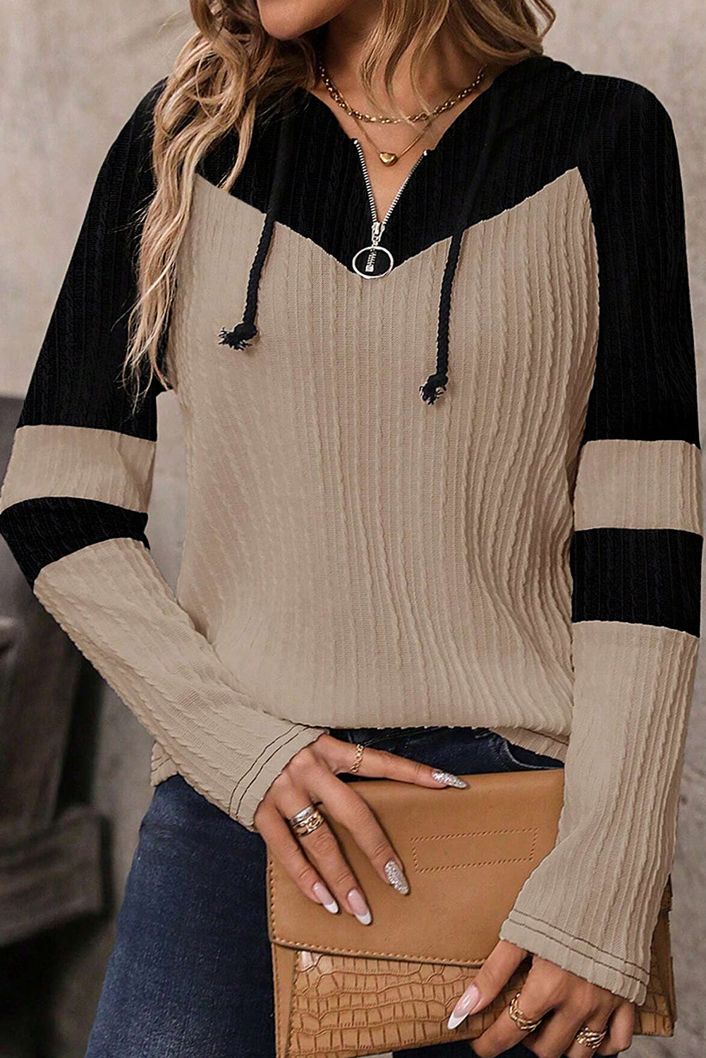 Person wearing a black and beige sweater holding a tan clutch.