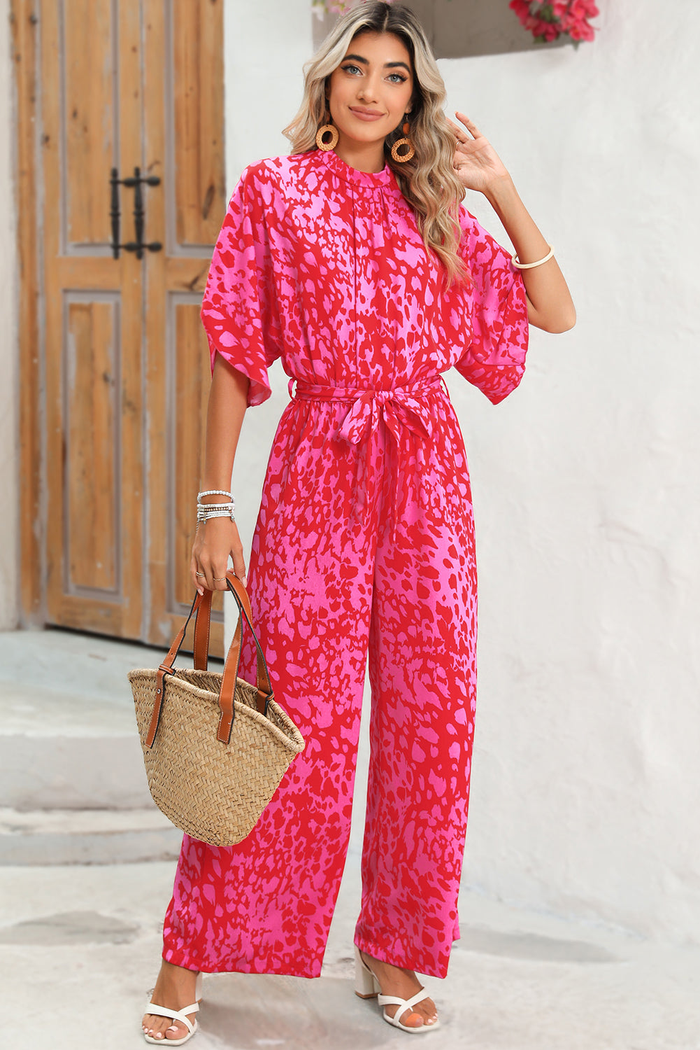 Woman wearing a pink patterned jumpsuit holding a straw bag.