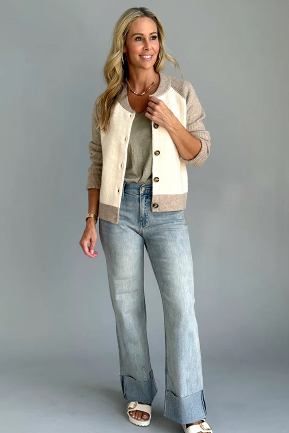 Woman wearing a beige cardigan, green top, and blue jeans against a gray background