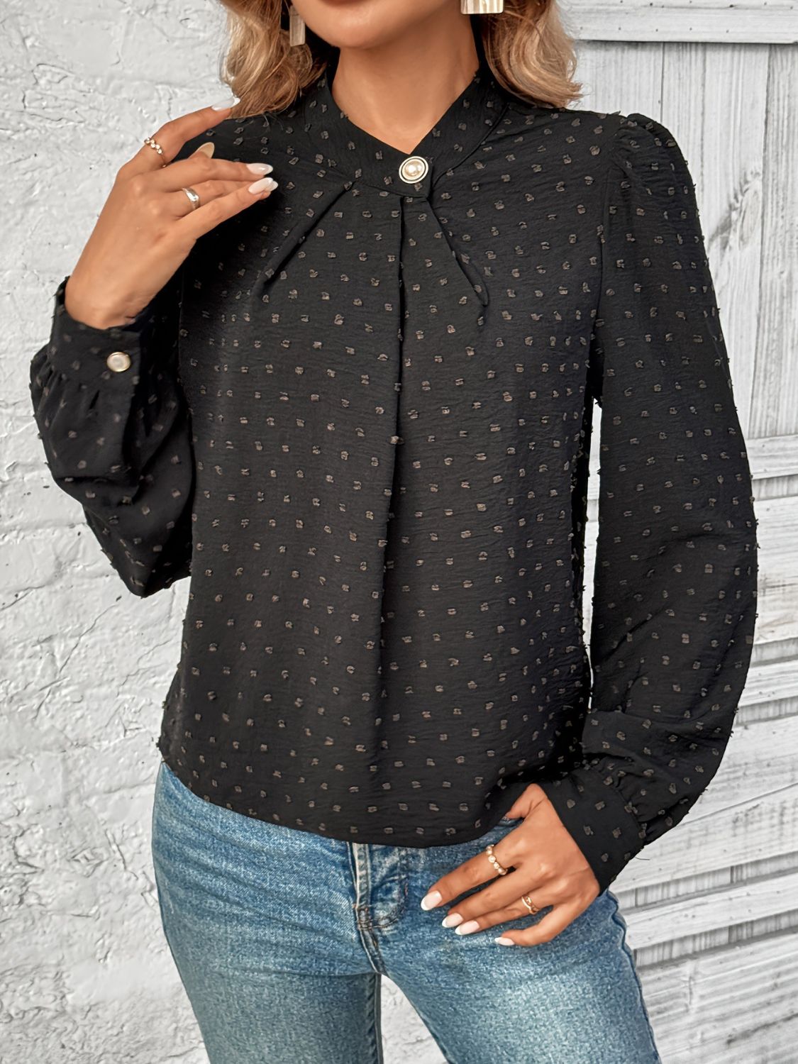 A woman wearing a black long sleeve blouse with a Swiss dot pattern and a mock neckline, close up 