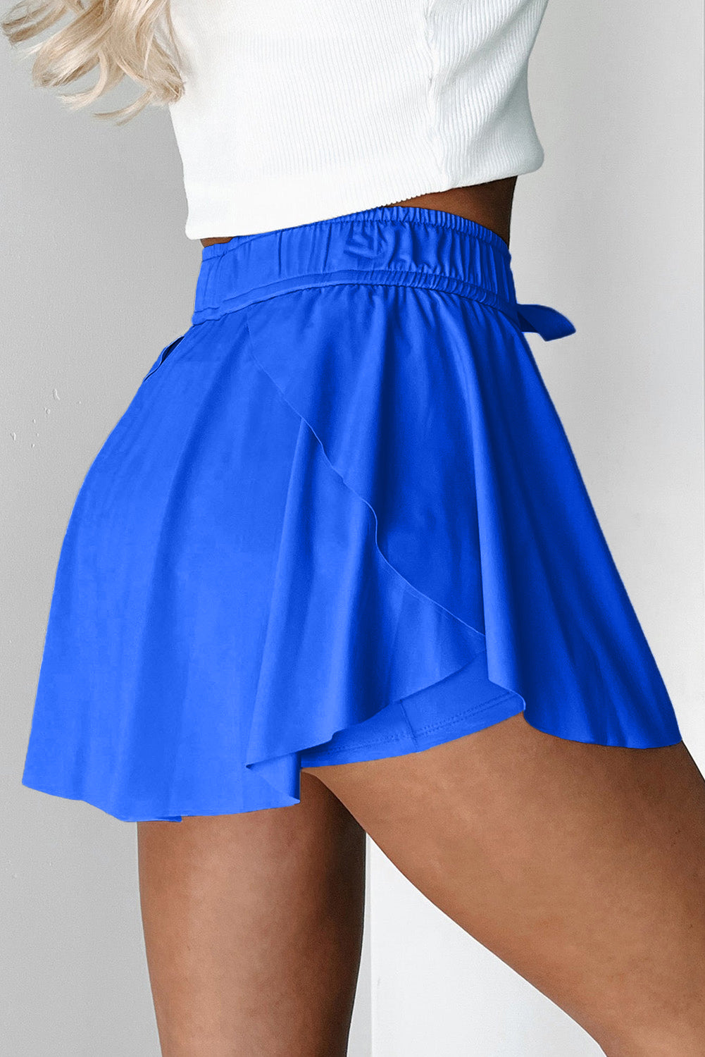 Blue tennis shorts worn by a person on a plain background side view