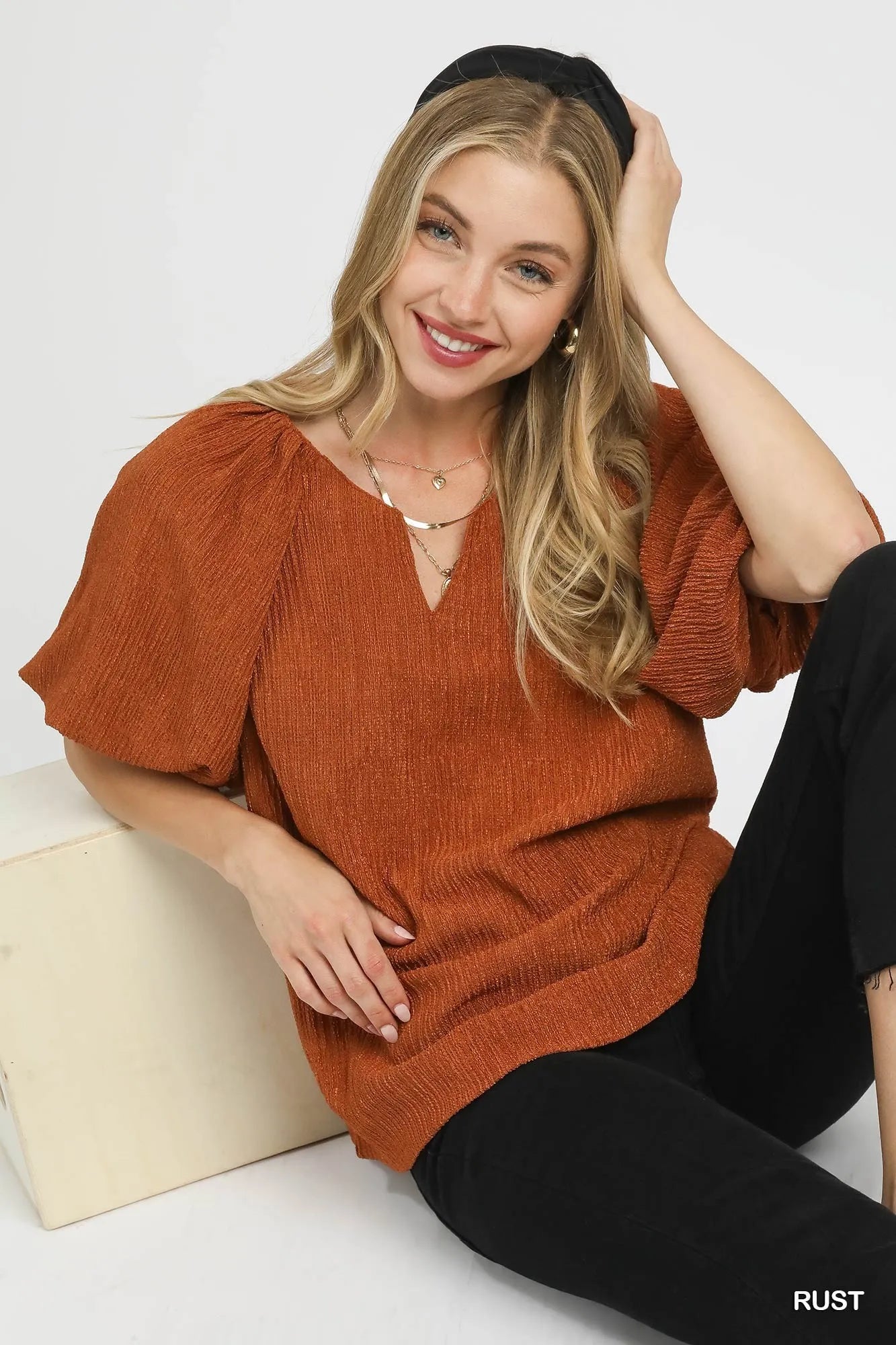 Woman wearing a rust-colored sweater sitting on a white surface with a plain background