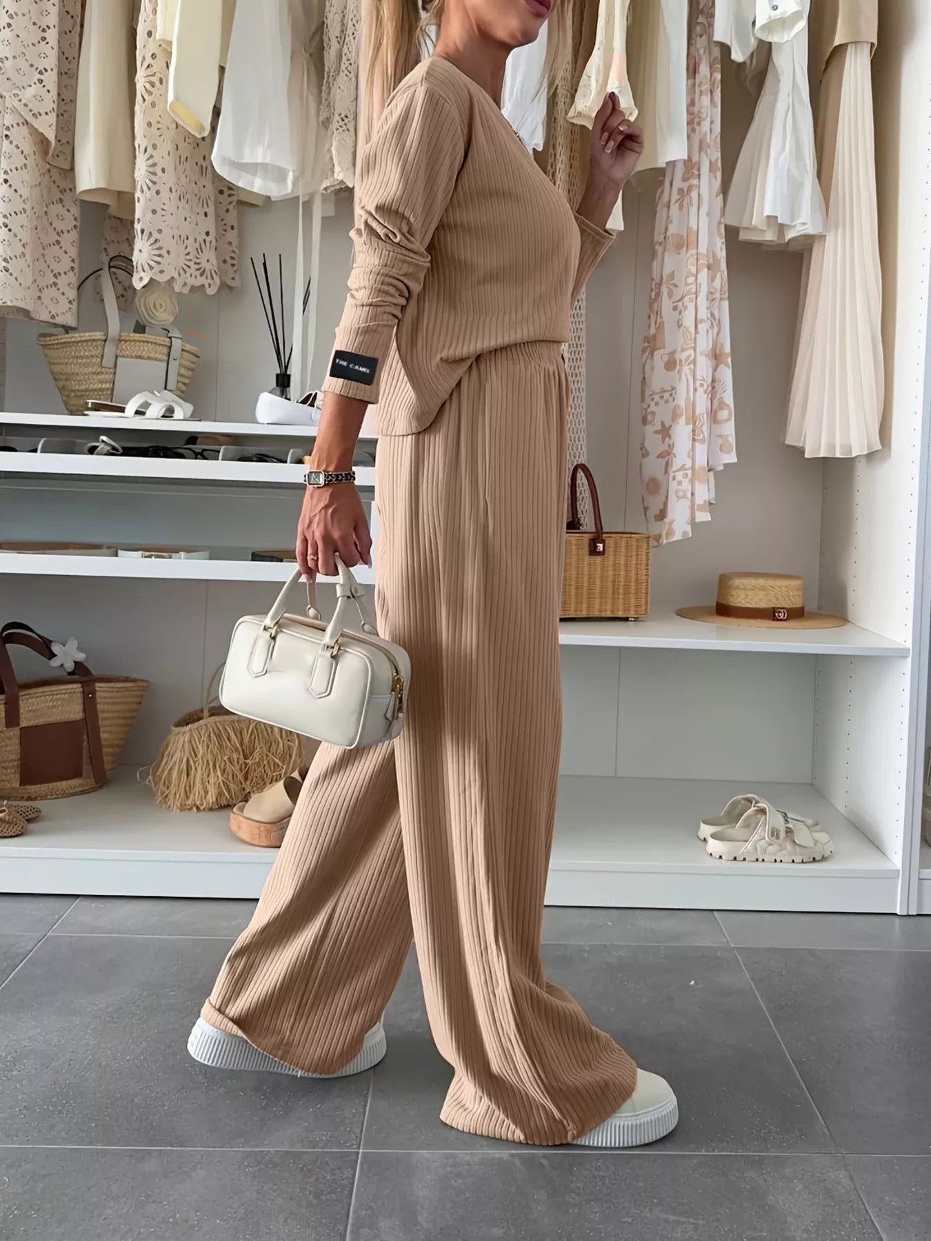 Person wearing a beige outfit holding a white handbag in a store setting.