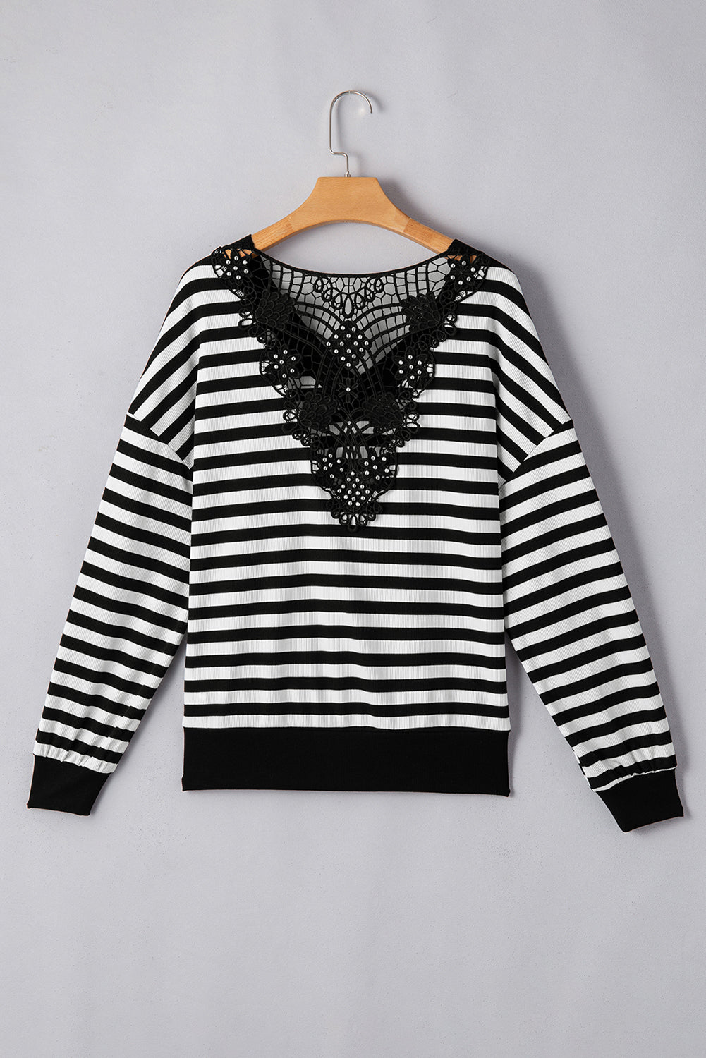 Black and white striped sweater with lace detail on a hanger against a gray background