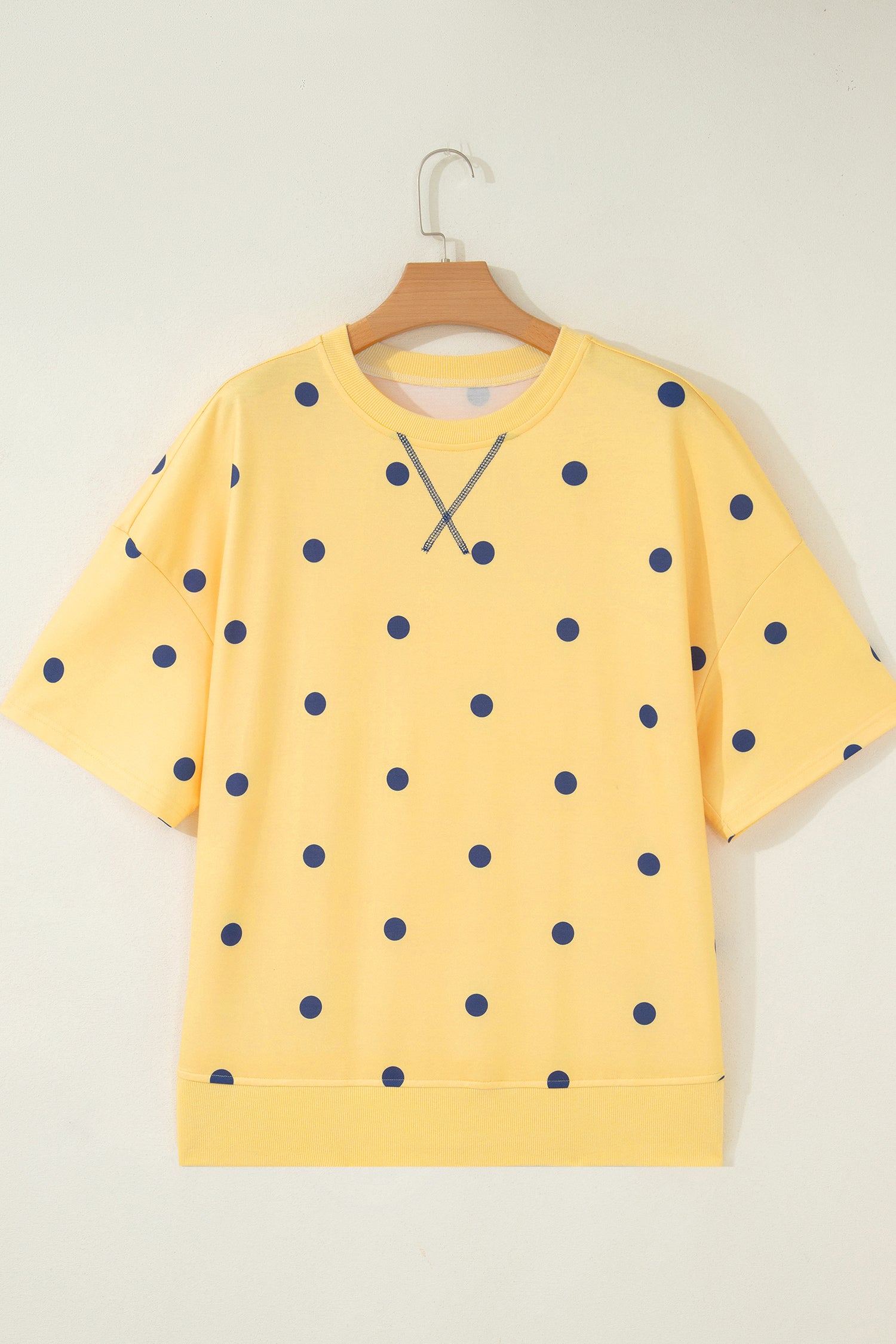 Yellow sweatshirt with blue polka dots on a wooden hanger against a white background front