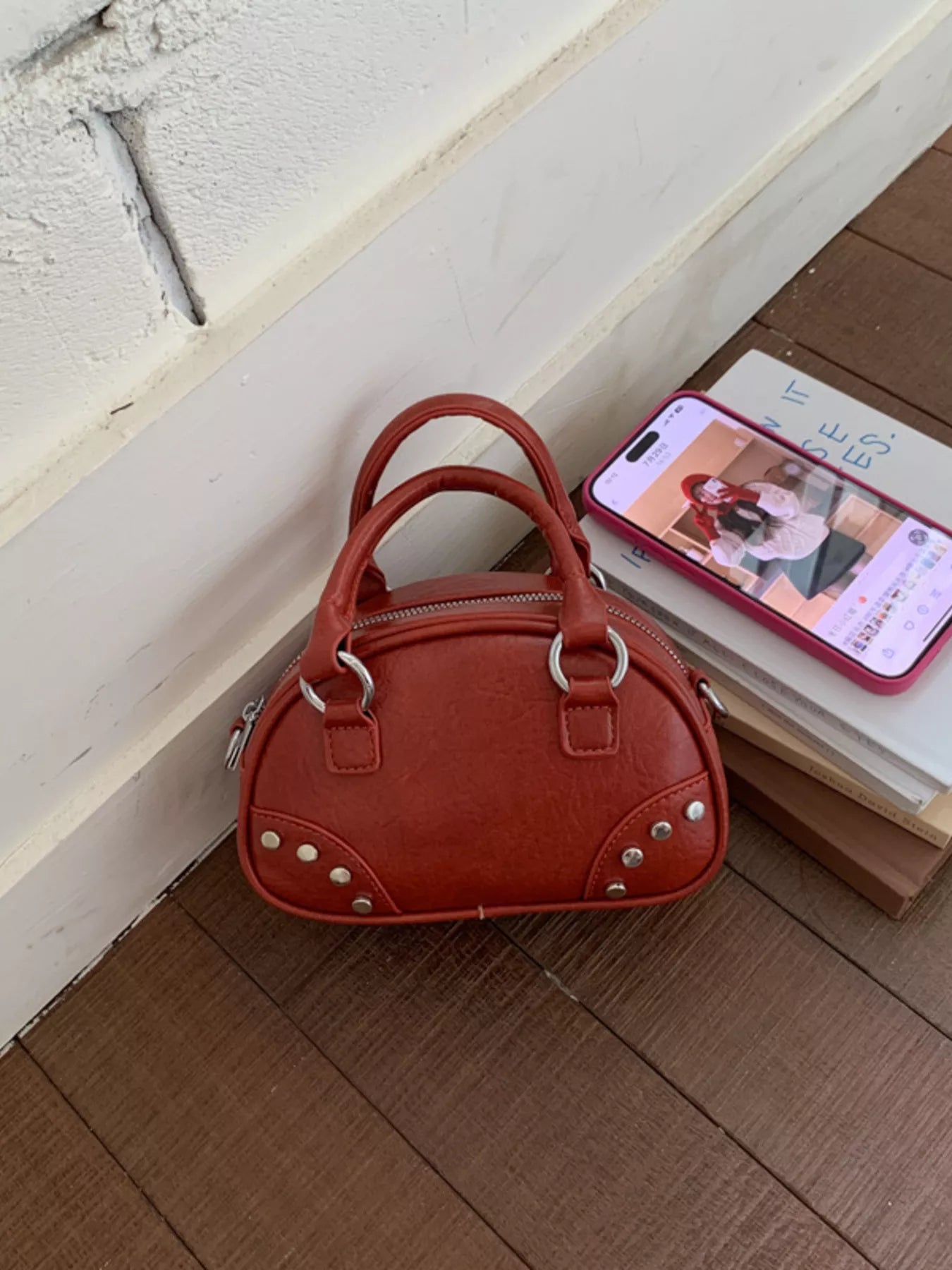 Red handbag on a wooden floor with a phone displaying a video call in the background.