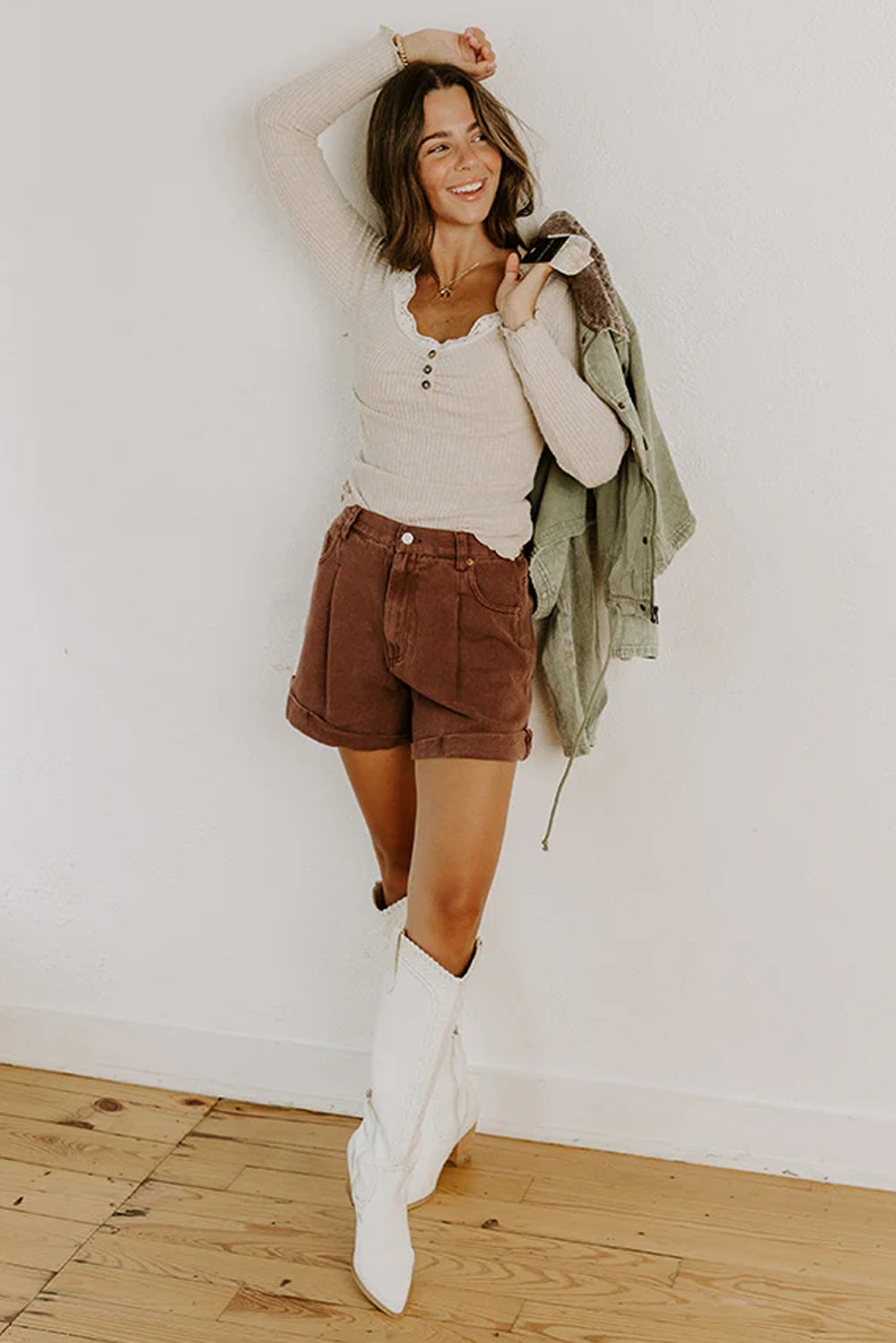 Woman in a casual outfit with shorts and a jacket against a white wall.
