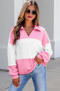 A woman wearing a Women's Rose Pink Colorblock Ruffle Trim Shift Sweatshirt  with scalloped trim, paired with blue jeans and sunglasses, standing outdoors against a light gray wall.