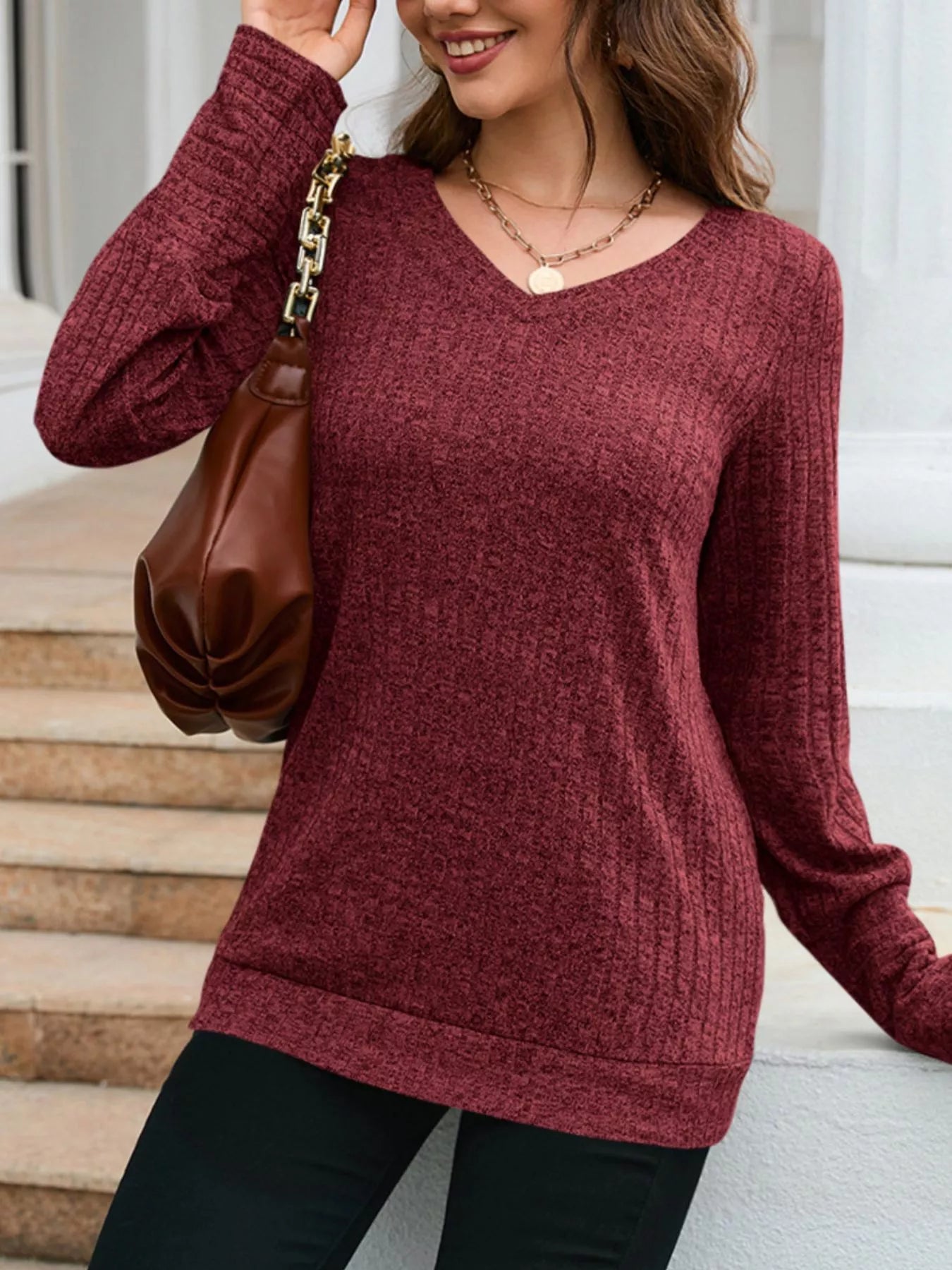Woman wearing a maroon sweater with a brown handbag on a neutral background