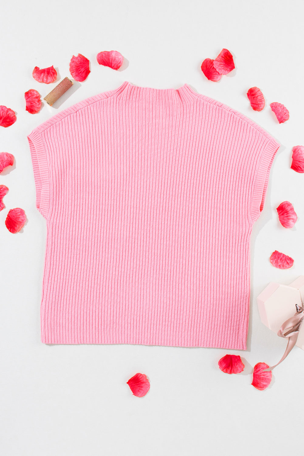 Pink ribbed sweater on a light gray background with scattered rose petals