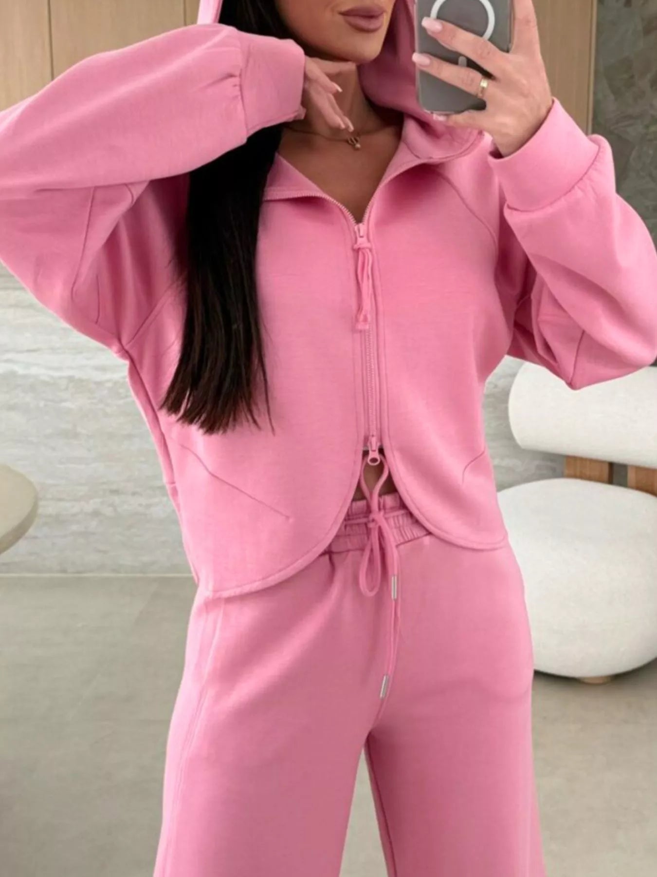 Person wearing a pink tracksuit taking a mirror selfie.