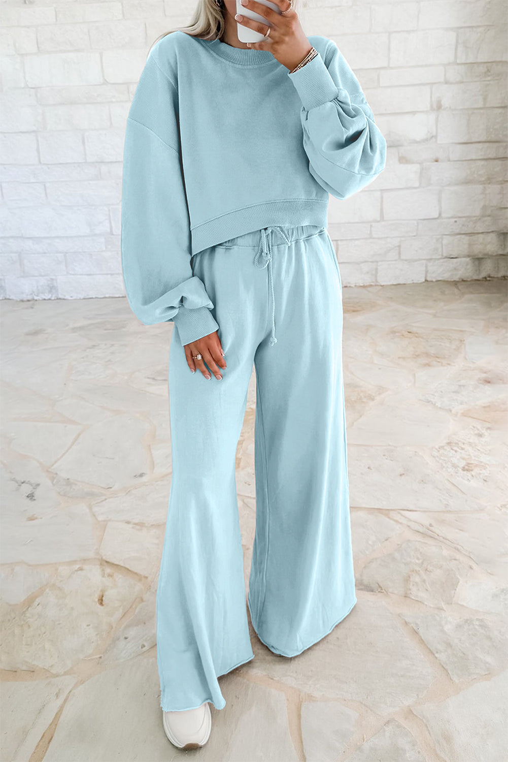 Person wearing a light blue outfit with wide-leg pants against a white brick wall.