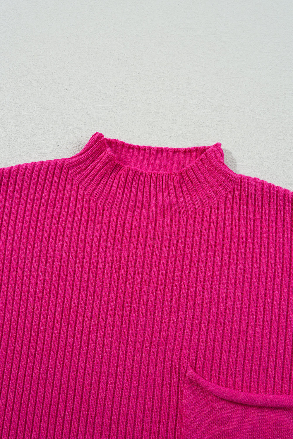 Close-up of a bright pink ribbed sweater on a light gray background