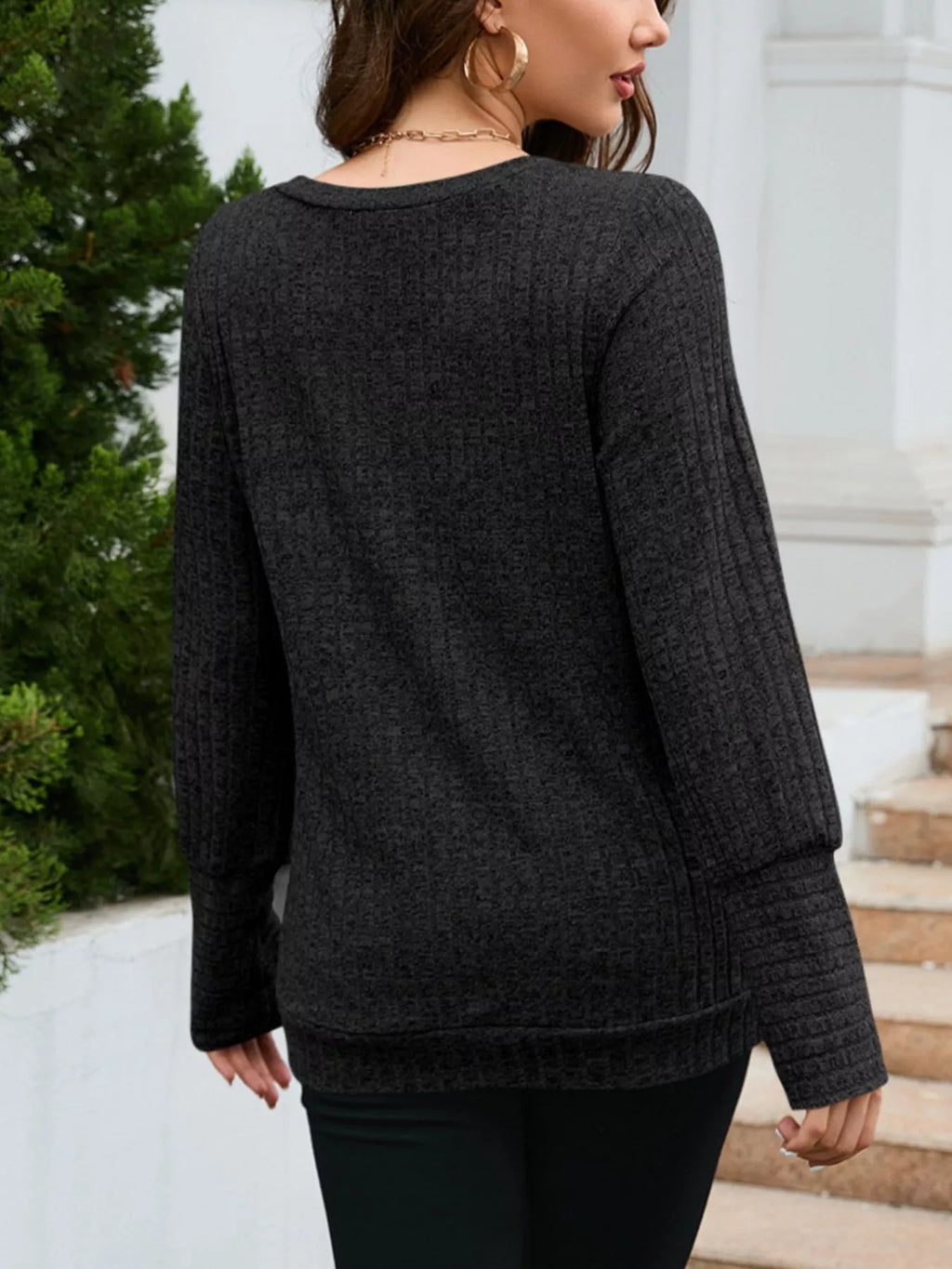 Woman wearing a dark gray sweater in an outdoor setting with steps and greenery.