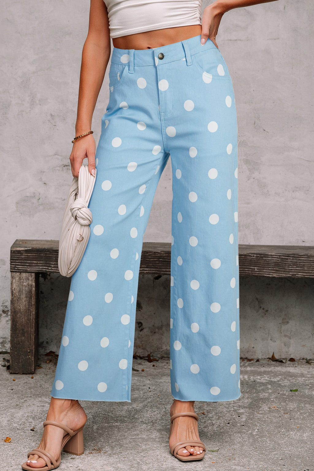 Person wearing light blue pants with white polka dots, standing against a concrete wall. Front view