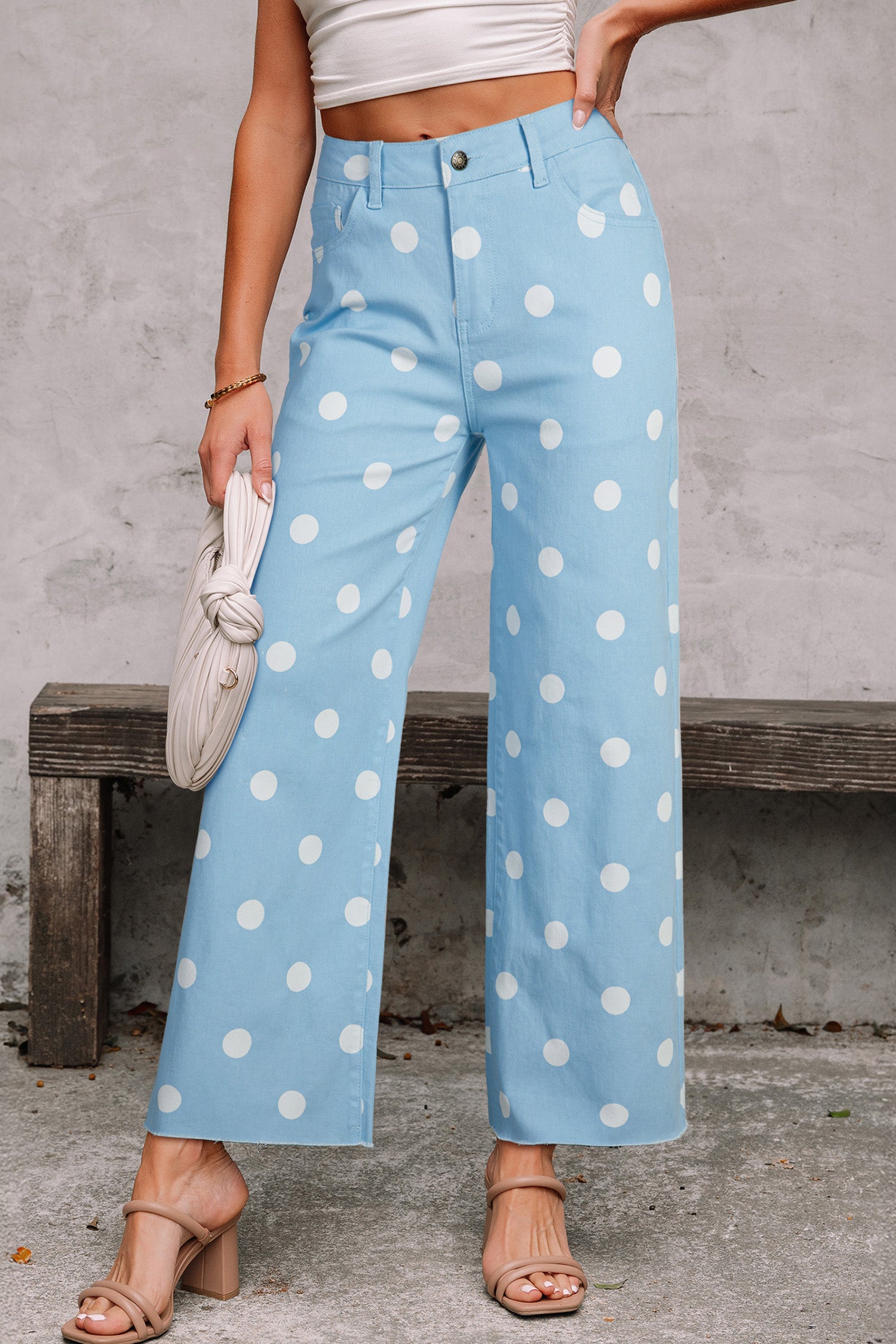 Person wearing light blue pants with white polka dots, standing against a concrete wall. Front view