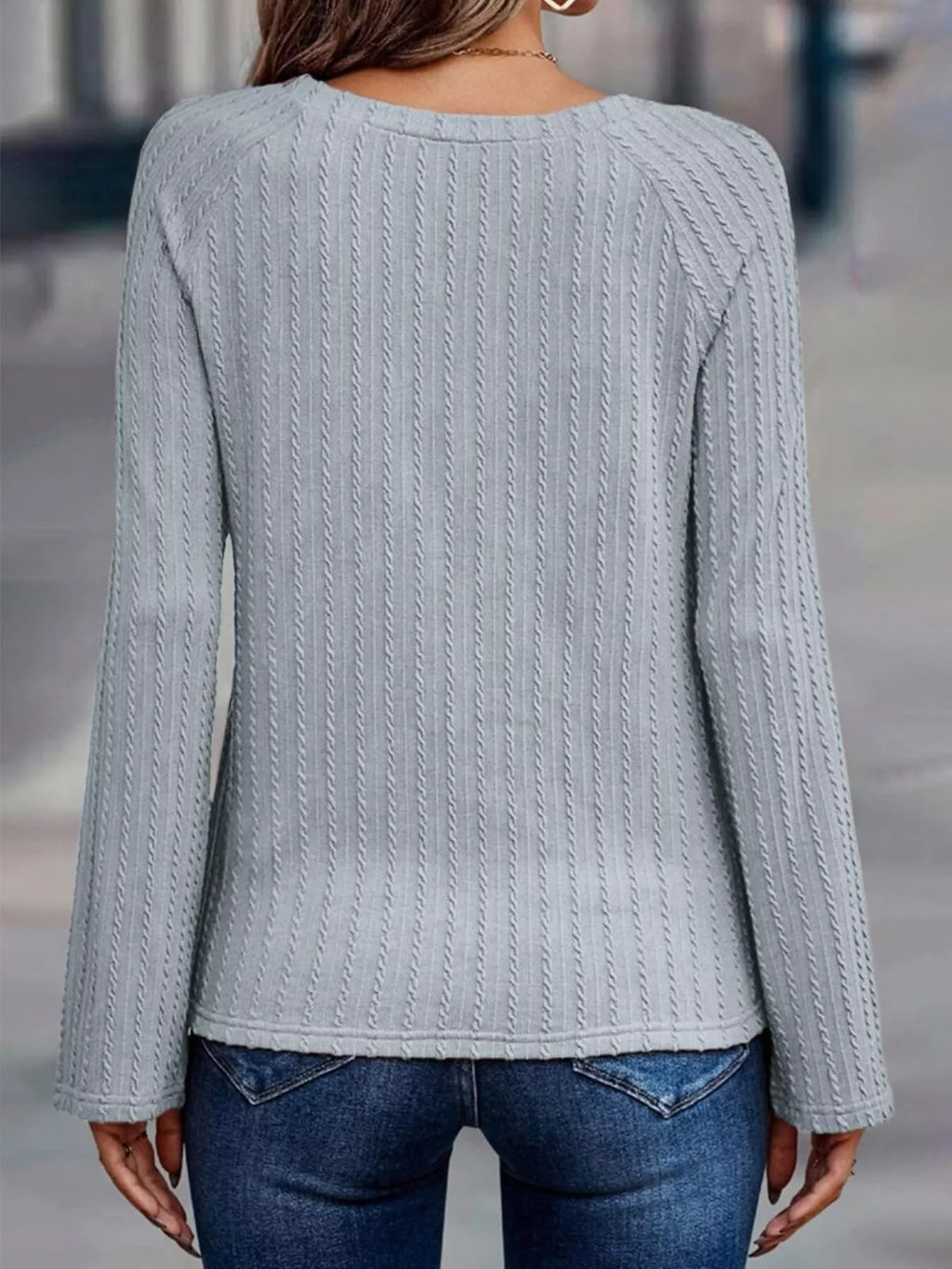 Person wearing a light gray cable knit sweater and blue jeans on a blurred street background