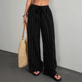 Person wearing black pinstripe pants holding a woven bag against a gray background
