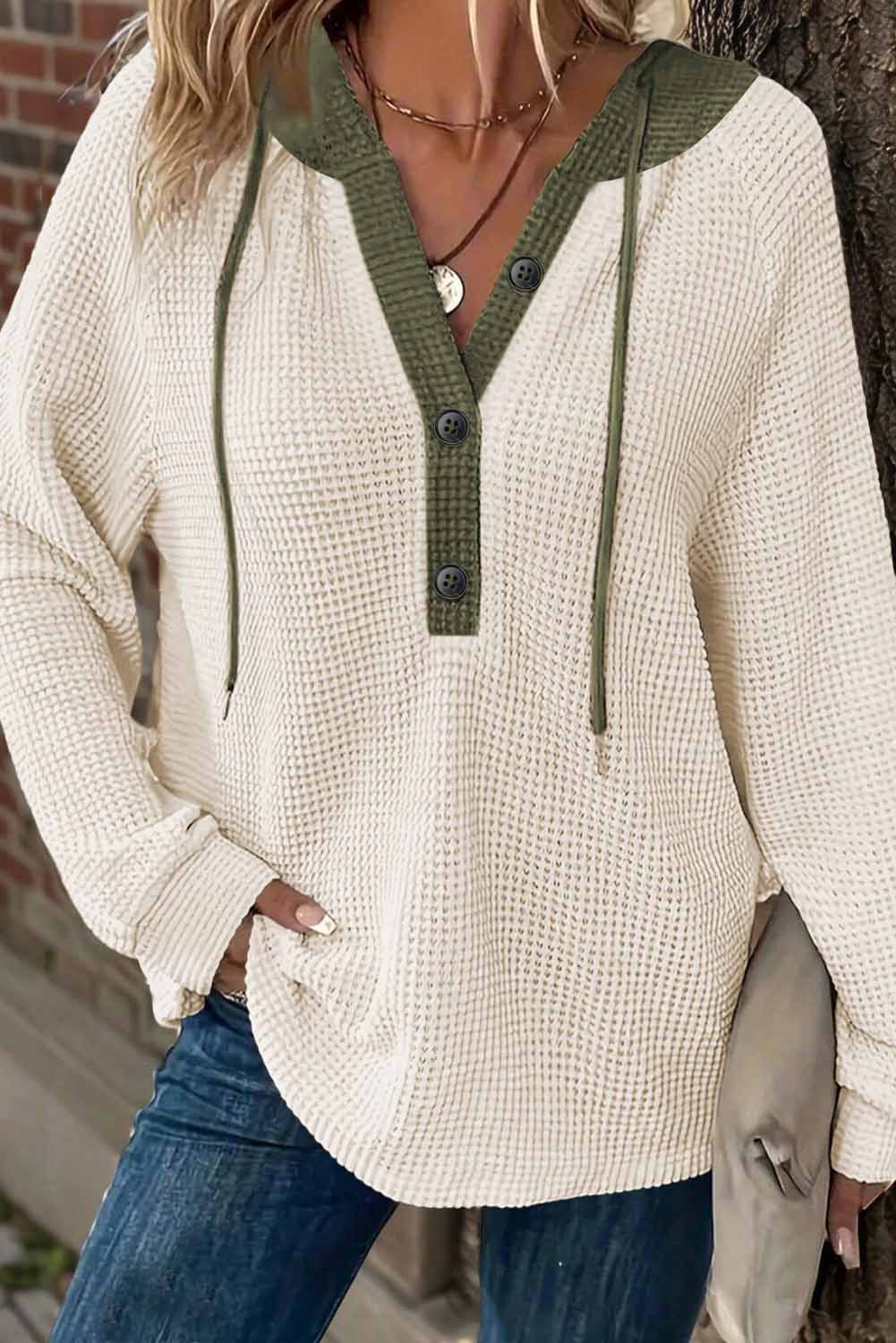 Person wearing a beige and green hoodie with a brick wall background