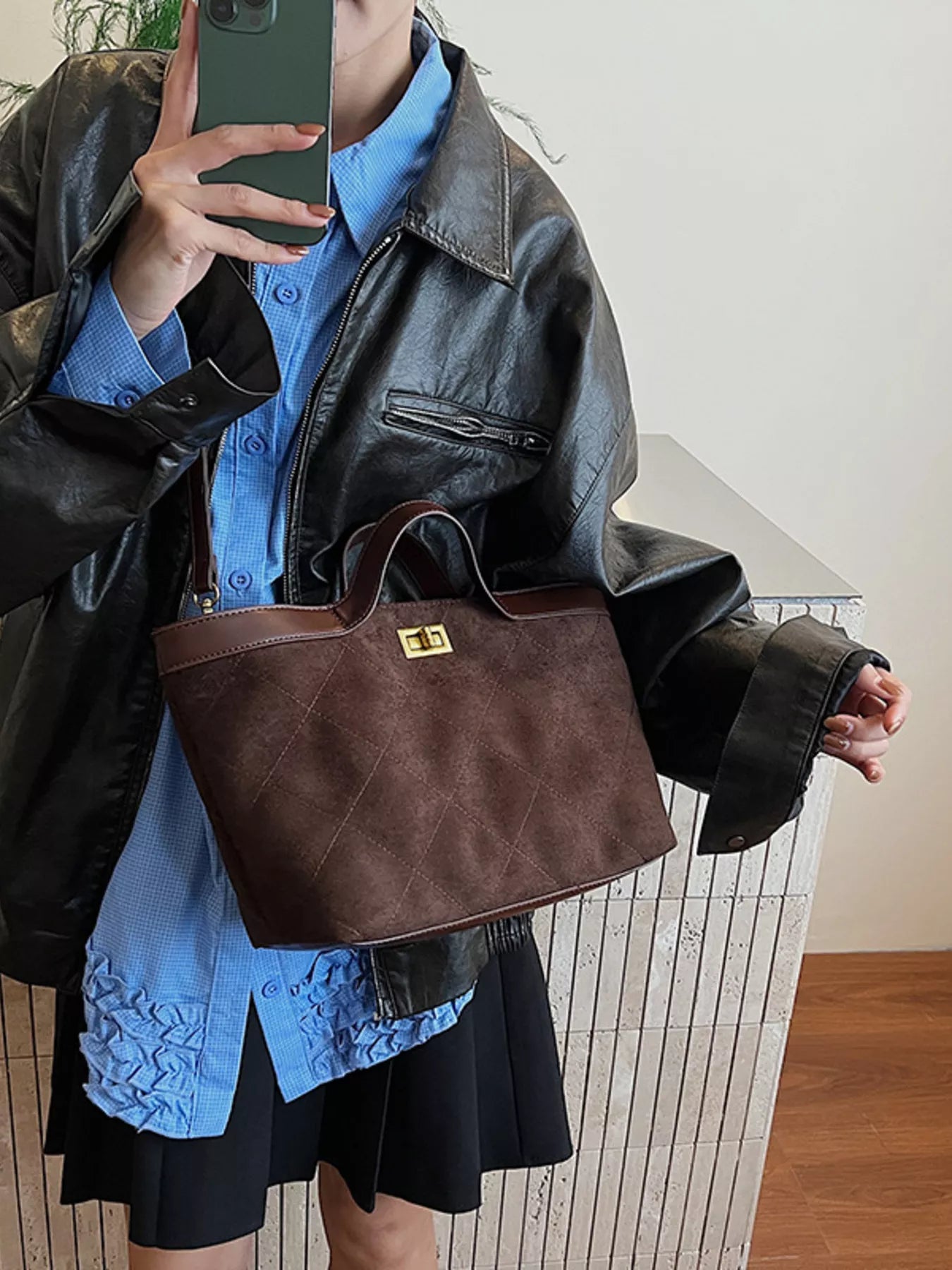 Person wearing a black leather jacket and blue shirt, holding a brown handbag.