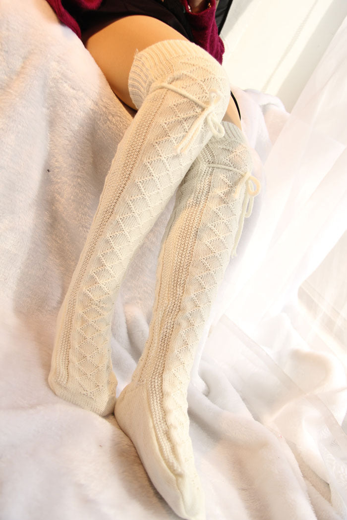 Beige knee-high socks with lace details worn by a person on a white blanket.
